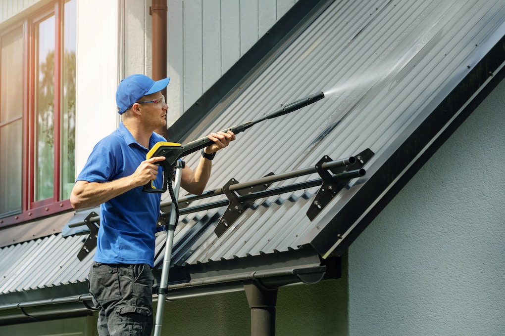 a man standing on a ladder spraying metal roof cleaner on roof